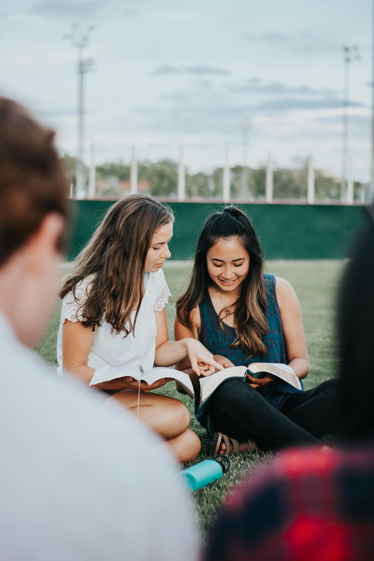 Two teenage girls smiling as they read their Bibles together outdoors